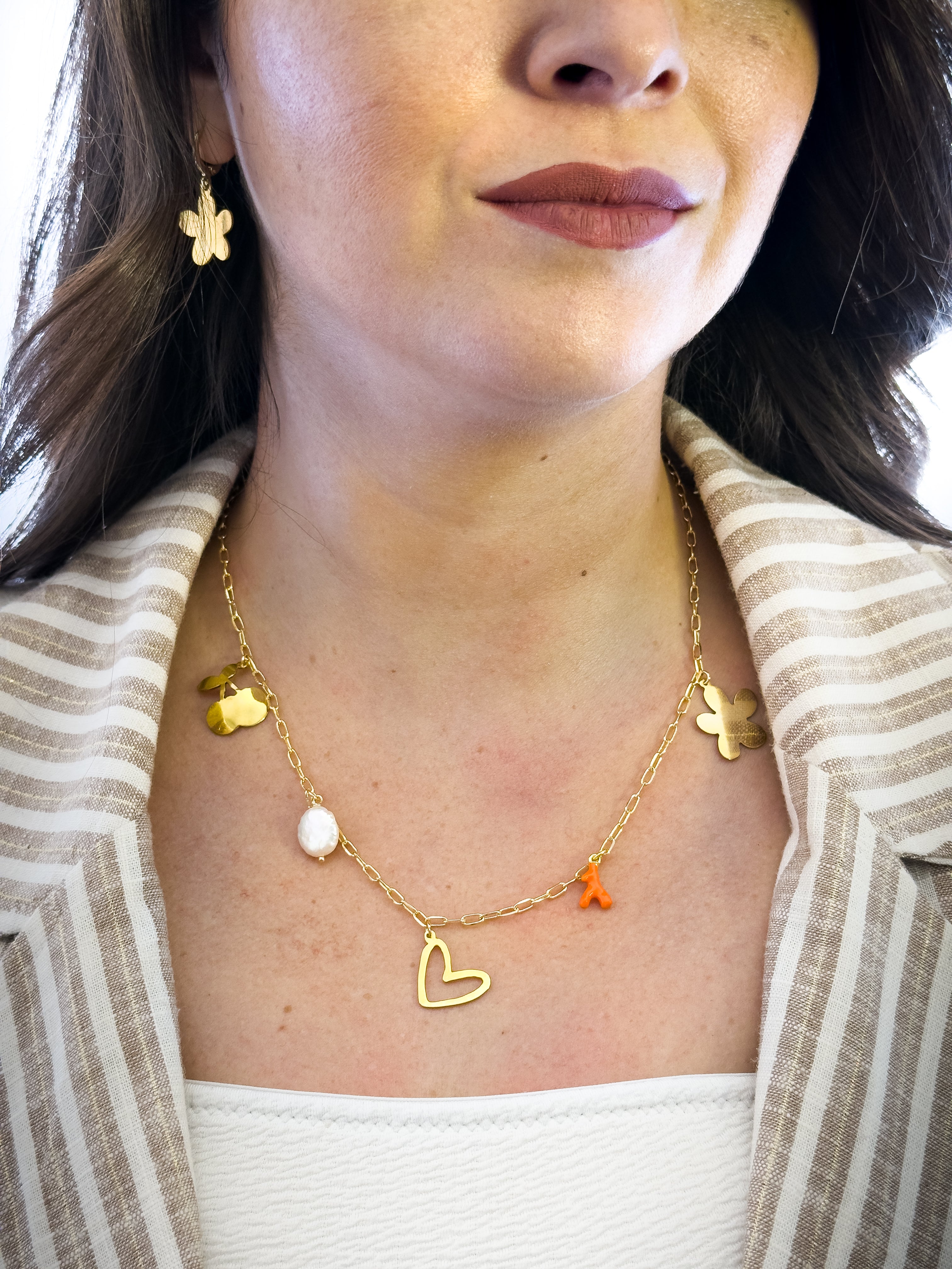 Modelo usando collar con corazón, perla natural y coral bañado en oro de MAVIS.