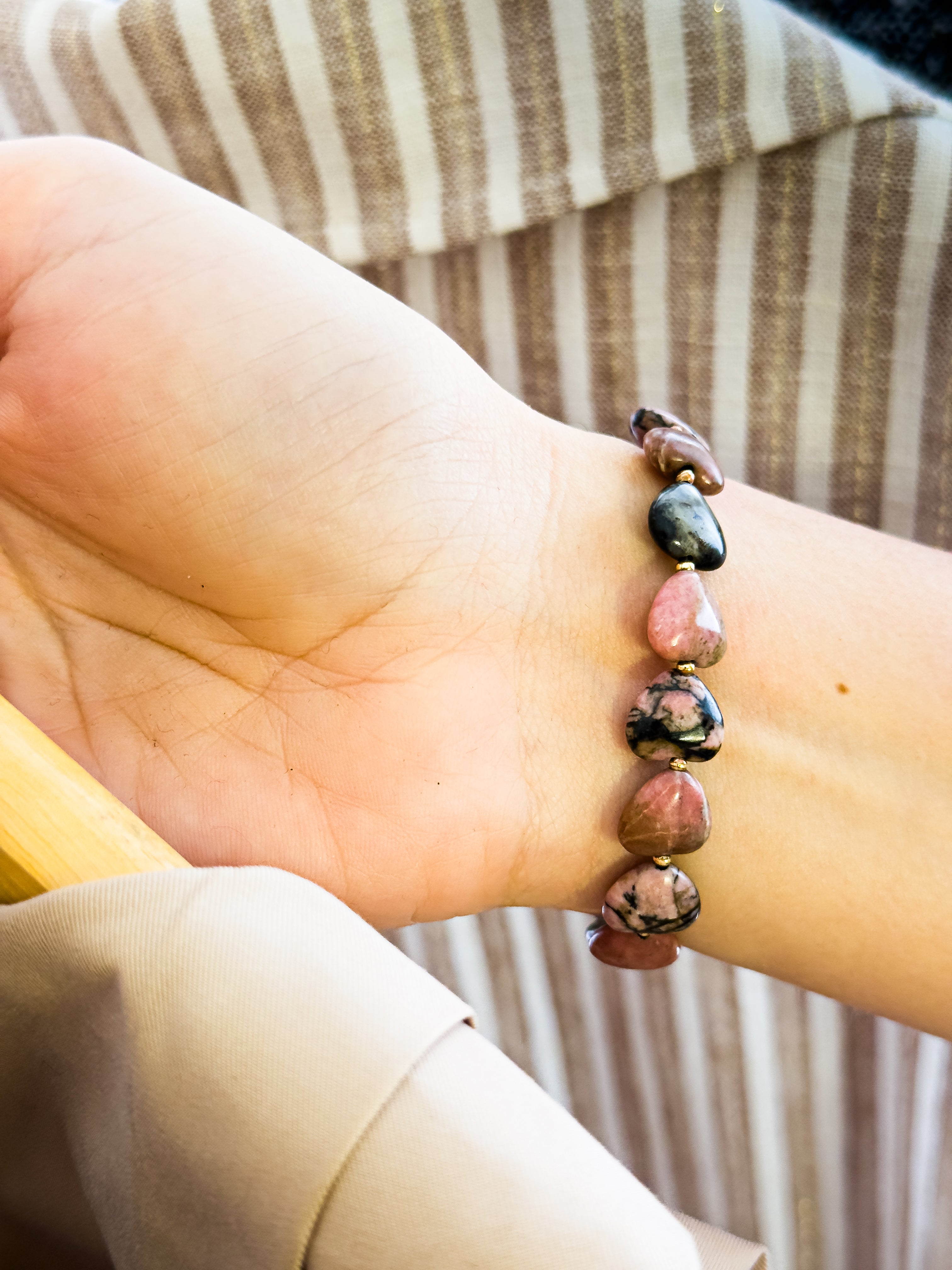Pulsera de Rodonita natural con corazones pulidos sobre la muñeca, mostrando el contraste natural entre los tonos rosados y las vetas negras