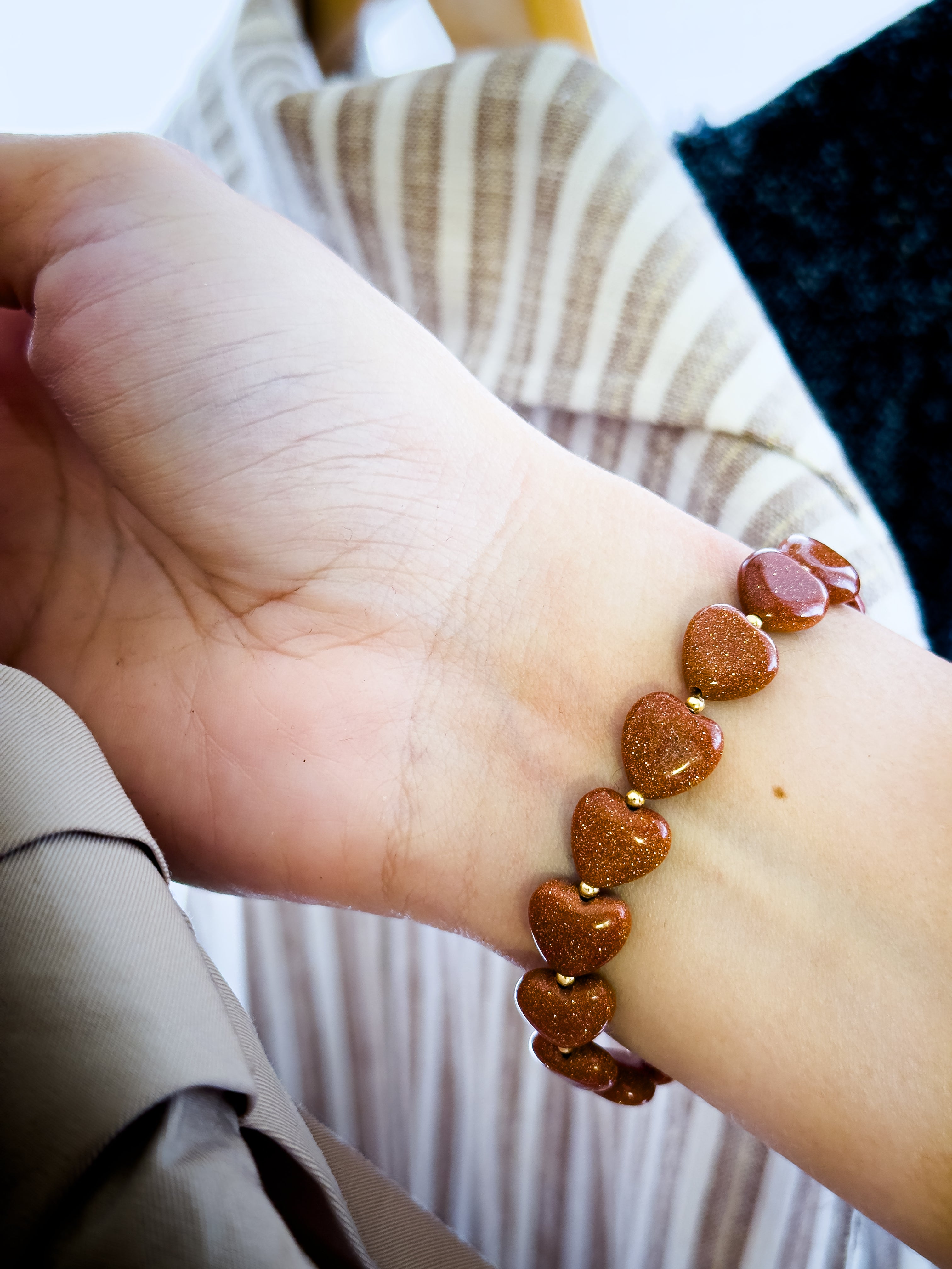 Pulsera de corazones Goldstone cobriza sobre la muñeca, destacando su intenso brillo con destellos dorados y diseño artesanal elegante.